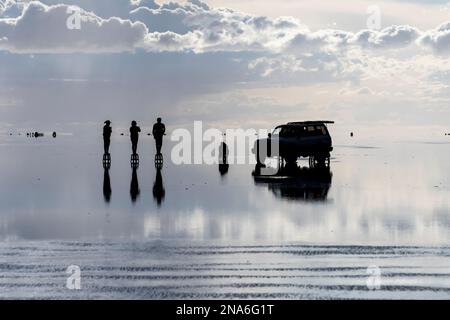 Touristes posant dans le reflet pendant la saison humide (décembre-février) dans le Salar de Uyuni, la plus grande plate-forme saline du monde Banque D'Images