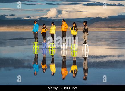 Touristes posant dans le reflet pendant la saison humide (décembre-février) dans le Salar de Uyuni, la plus grande plate-forme saline du monde Banque D'Images