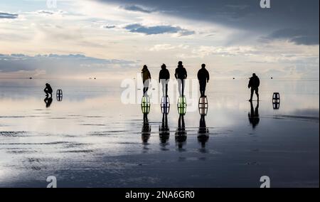 Touristes posant dans le reflet pendant la saison humide (décembre-février) dans le Salar de Uyuni, la plus grande plate-forme saline du monde Banque D'Images