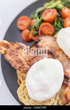 Petit déjeuner copieux, œufs pochés avec bacon sur pain grillé, tomates frites et épinards Banque D'Images