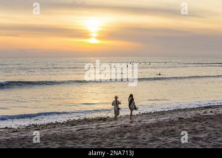 Surfeurs dans l'eau et gens marchant sur la plage au coucher du soleil, San Onofre State Beach ; San Clemente, Californie, États-Unis Banque D'Images