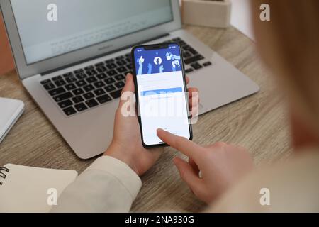 MYKOLAIV, UKRAINE - 28 AOÛT 2020: Femme tenant l'iPhone 11 avec l'application Facebook à l'écran à table, gros plan Banque D'Images
