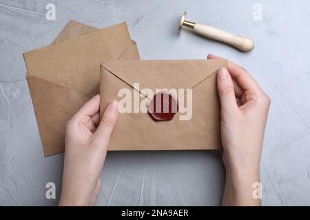 Femme tenant une enveloppe avec un sceau de cire sur une table grise, vue du dessus Banque D'Images