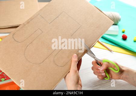 Femme coupant la forme de cactus à partir de papier de carton à table blanche en bois, gros plan. Pinata DIY Banque D'Images