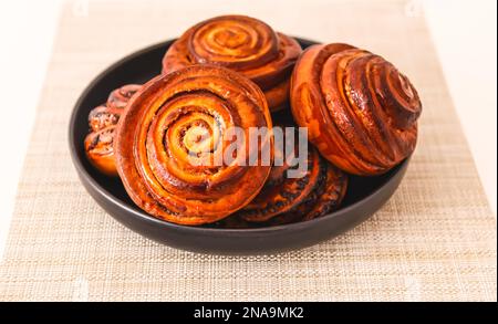 Petits pains à la cannelle faits maison sur une assiette en céramique noire. Banque D'Images