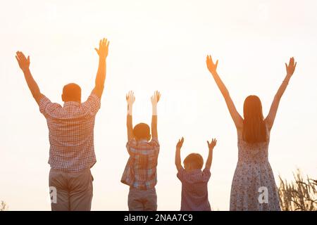 Les silhouettes des parents et des enfants élèvent les mains vers le ciel Banque D'Images