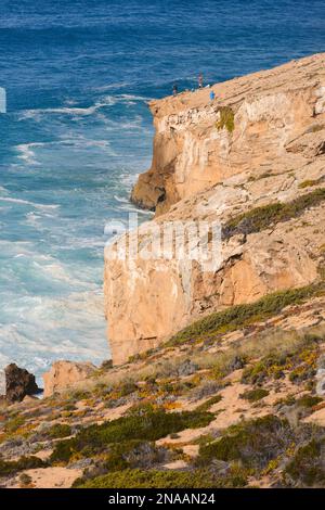 Les touristes se tiennent sur une crête escarpée en pente surplombant les falaises et le littoral de l'océan Atlantique, Praia de Monte Clerigo et le sud-ouest de l'Alentejo et ... Banque D'Images