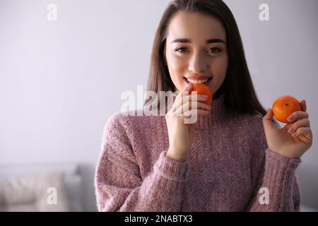 Bonne jeune femme avec des mandarines fraîches et mûres à la maison Banque D'Images