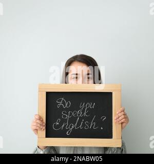 Jeune enseignante tenant un tableau noir avec des mots Parlez-vous anglais ? sur fond clair. Espace pour le texte Banque D'Images