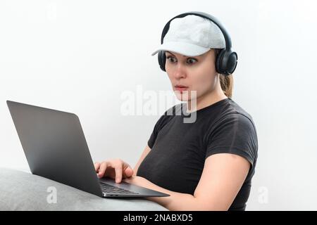 Une jeune femme active dans un casque qui travaille sur un ordinateur portable, qui fait des appels vidéo et regarde l'écran d'un ordinateur portable avec des émotions positives. Banque D'Images