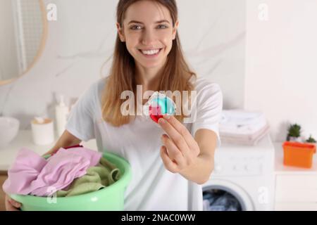 Femme tenant des vêtements sales et la capsule de détergent à lessive dans la salle de bains, se concentrer sur la main Banque D'Images