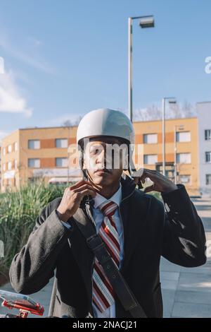 Jeune homme d'affaires mettant un casque à cheval sur un scooter électrique Banque D'Images