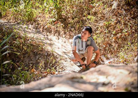 Beau homme asiatique avec équipement de trekking nouant ses lacets, trekking sur le sentier de montagne rocailleux le jour ensoleillé. concept d'activité extérieure Banque D'Images