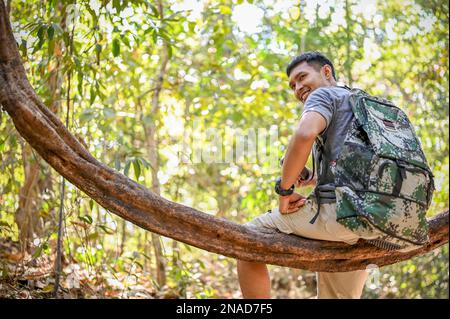 Un bon petit trekker ou voyageur asiatique se trouve sur une vigne en bois, se reposant en trekking dans la forêt. aventure, activités de plein air, exploration Banque D'Images