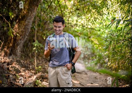 Joyeux et souriant asiatique mâle trekker ou voyageur avec un sac à dos regardant la route de trekking sur la carte, aime marcher le sentier dans les montagnes. Banque D'Images