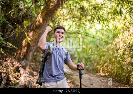 Joyeux et joyeux homme de voyage asiatique ou trekker avec l'équipement de trekking et sac à dos de la main vers le haut du geste de triomphe, célébrant le succès, est arrivé à la destinati Banque D'Images