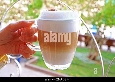 Main de femme tenant un verre de cappuccino mousseux appétissant Banque D'Images