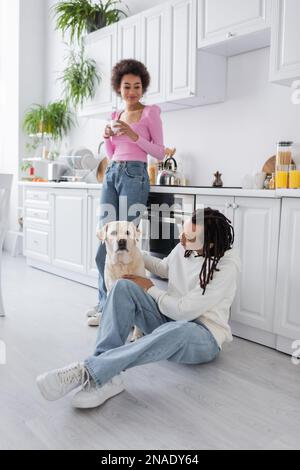 Afro-américain tenant du café près d'un petit ami pétant le labrador dans la cuisine Banque D'Images