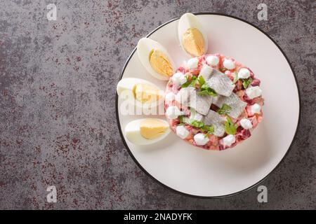 Salade de hareng avec betteraves, pommes, pommes de terre et oignons dans une assiette sur la table. Vue horizontale du dessus Banque D'Images