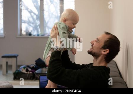 Papa tient le bébé devant lui dans les bras et sourit Banque D'Images