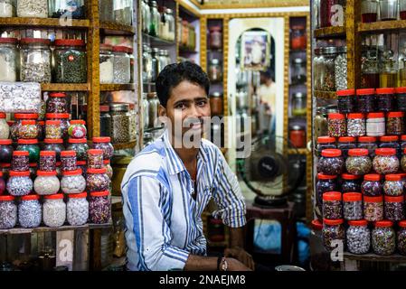 Commerçant masculin assis dans sa boutique pleine de pots de bonbons ; Varanasi, Inde Banque D'Images