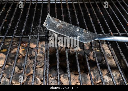 Nettoyer un gril sale en se tenant sur la terrasse et en vidant les cendres. Banque D'Images