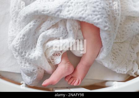 Fines jambes du nouveau-né dans une couverture. Entourez le couvre-lit autour des pieds de bébé. Un enfant recouvert d'une couverture tricotée en dentelle. Banque D'Images