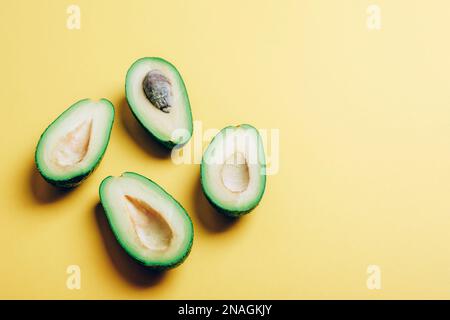 Moitiés d'avocat sur fond jaune avec des ombres nettes. Concept alimentaire végétalien sain. Vue de dessus, espace de copie. Banque D'Images