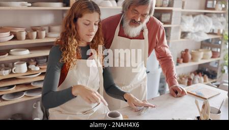 Professeur d'art, poterie et homme senior dans une classe, conseils d'apprentissage dans la classe d'art. Jeune femme enseignant le vieil homme à rouler l'argile, la sculpture et le don Banque D'Images