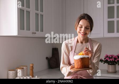 Jeune femme avec gâteau traditionnel décoré de Pâques dans la cuisine, espace pour le texte Banque D'Images