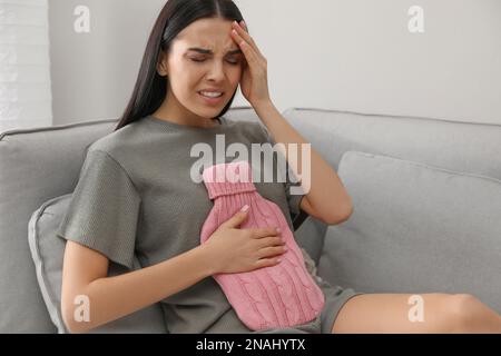 Femme utilisant un flacon d'eau chaude pour soulager la douleur abdominale à la maison Banque D'Images