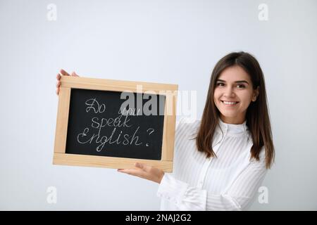 Jeune enseignante tenant un tableau noir avec des mots Parlez-vous anglais ? sur fond clair Banque D'Images