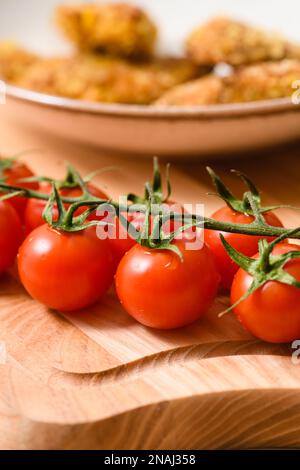 Branche fraîche de tomates cerises sur le fond d'un plat avec des nuggets de poulet. Gros plan. Banque D'Images