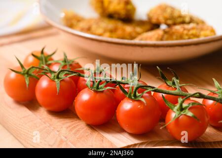 Branche fraîche de tomates cerises sur le fond d'un plat avec des nuggets de poulet. Gros plan. Banque D'Images