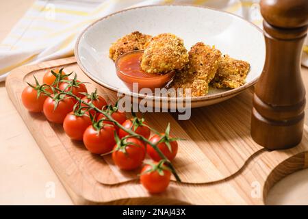 Nuggets de poulet faits maison avec tomates cerises et ketchup sur une planche en bois, gros plan Banque D'Images