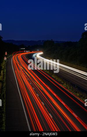 Les voitures qui se déplacent rapidement sur l'autoroute M5 laissent des sentiers de signalisation et des traînées de lumière lorsqu'elles passent le long d'une autoroute très fréquentée Banque D'Images