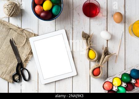 Préparations de Pâques et teintures pour oeufs. Œufs de pâques colorés et œufs de lapin avec tablette numérique sur fond de bois. Directement au-dessus du plan d'examen. Banque D'Images