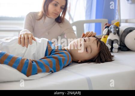 Enfant préadolescent, garçon, allongé à l'hôpital avec une colonne thoracique fracturée, vertébrés, mère assise à côté de son lit Banque D'Images