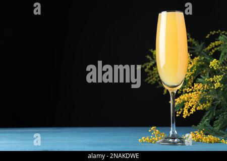 Verre de Mimosa cocktail avec branches fleuries sur table en bois bleu clair. Espace pour le texte Banque D'Images