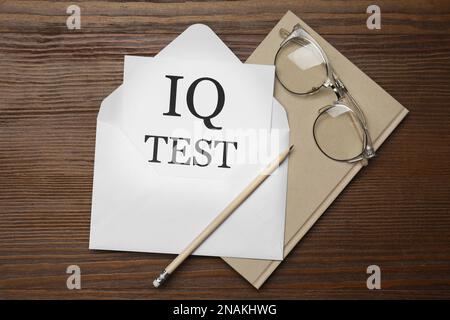 Papier avec mots IQ Test dans une enveloppe, un crayon, un carnet et des lunettes sur une table en bois, à plat Banque D'Images