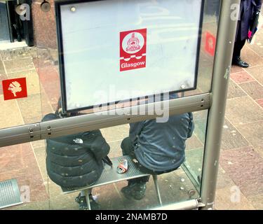 2 passagers à un arrêt de bus sous le logo du conseil municipal de Glasgow, symbole de cloche emblématique de son mythe Banque D'Images