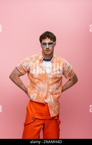 Homme élégant en lunettes de soleil et pose globale isolée sur rose, image de stock Banque D'Images