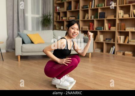 Sport et régime sain pour la perte de poids concept. Jeune femme coréenne assise sur une balance et faisant un geste YES Banque D'Images