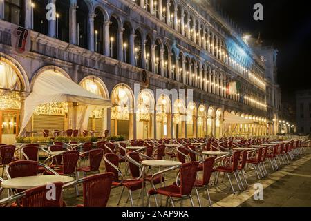 Venise, Italie Vider la place Saint-Marc avec des arcades la nuit. Magasins fermés avec chaises rouges vides empilées autour des tables, à l'emblématique Piazza San Marco Banque D'Images