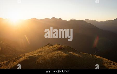 Panorama au coucher du soleil de rouge idyllique isolé montagne alpine Brewster Hut perché au sommet de la colline de l'herbe au-dessus de la vallée de la rivière Haast, West Coast SO Banque D'Images