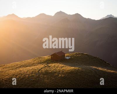 Panorama au coucher du soleil de rouge idyllique isolé montagne alpine Brewster Hut perché au sommet de la colline de l'herbe au-dessus de la vallée de la rivière Haast, West Coast SO Banque D'Images