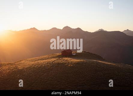 Panorama au coucher du soleil de rouge idyllique isolé montagne alpine Brewster Hut perché au sommet de la colline de l'herbe au-dessus de la vallée de la rivière Haast, West Coast SO Banque D'Images