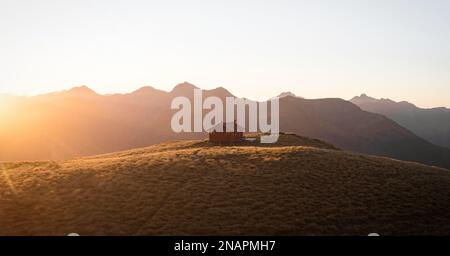 Panorama au coucher du soleil de rouge idyllique isolé montagne alpine Brewster Hut perché au sommet de la colline de l'herbe au-dessus de la vallée de la rivière Haast, West Coast SO Banque D'Images