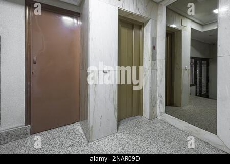 Intérieur d'un portail résidentiel avec ascenseur avec portes en métal vert, miroirs et sol en granit gris Banque D'Images