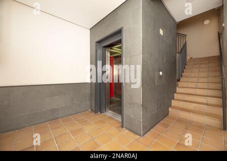 Intérieur d'un portail résidentiel avec ascenseur avec portes métalliques ouvertes, escaliers et sol en grès brun Banque D'Images